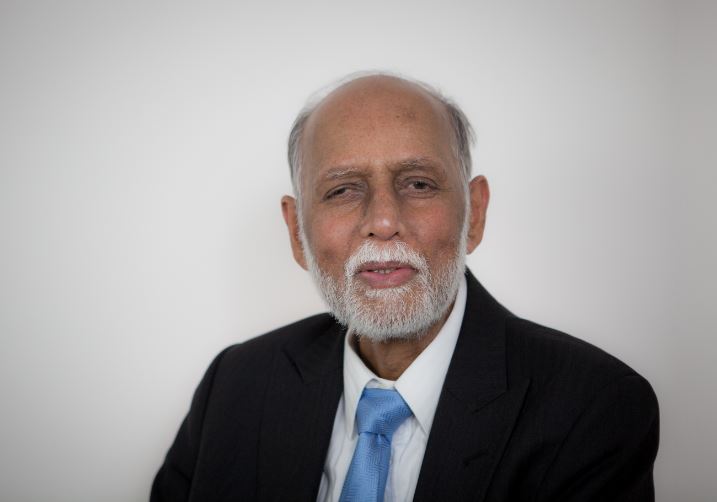 An image of Raj Mehta, an older Asian man wearing a black suit and blue tie. He is looking at the camera with a smile.